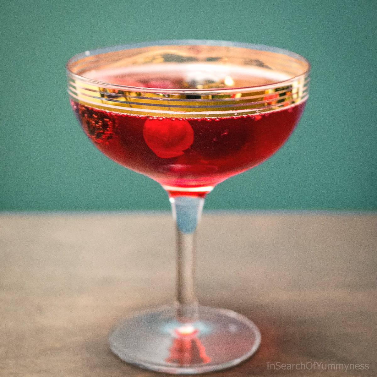 A coupe glass of sparkling cranberry punch with frozen berries floating inside.
