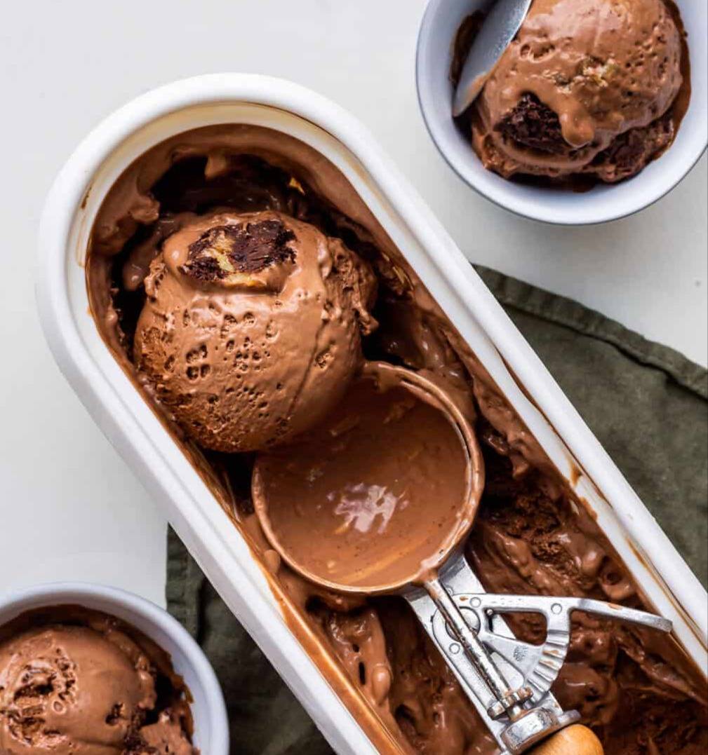 A scoop of chocolate brownie ice cream in a container with an ice cream scoop.