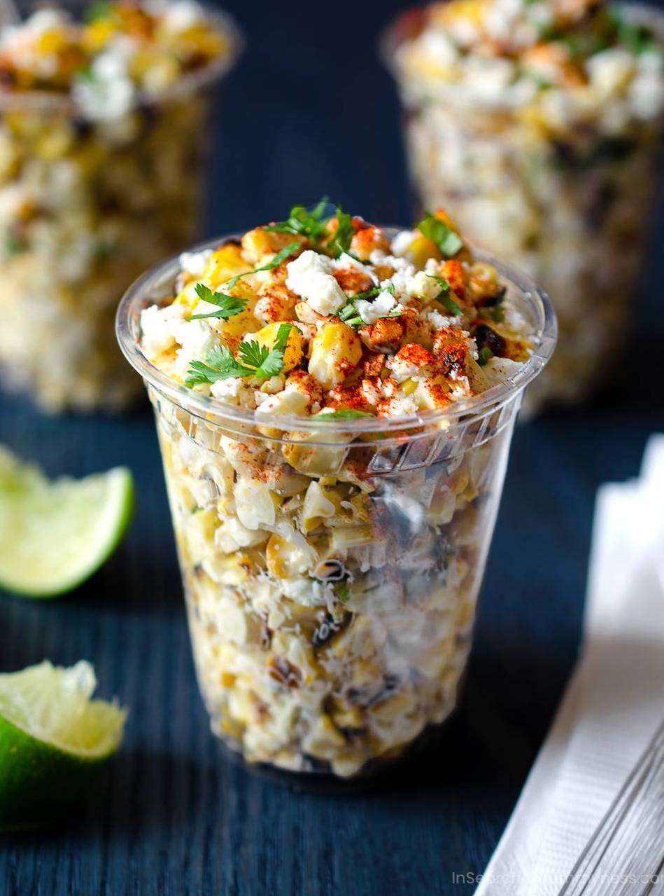 A clear cup full of Mexican-style corn with cheese.