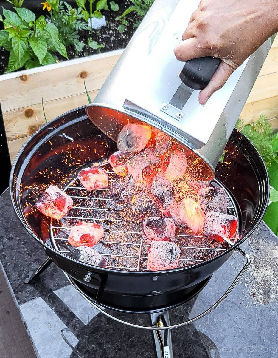 Hot coals being dumped onto a charcoal grate from a charcoal chimney.