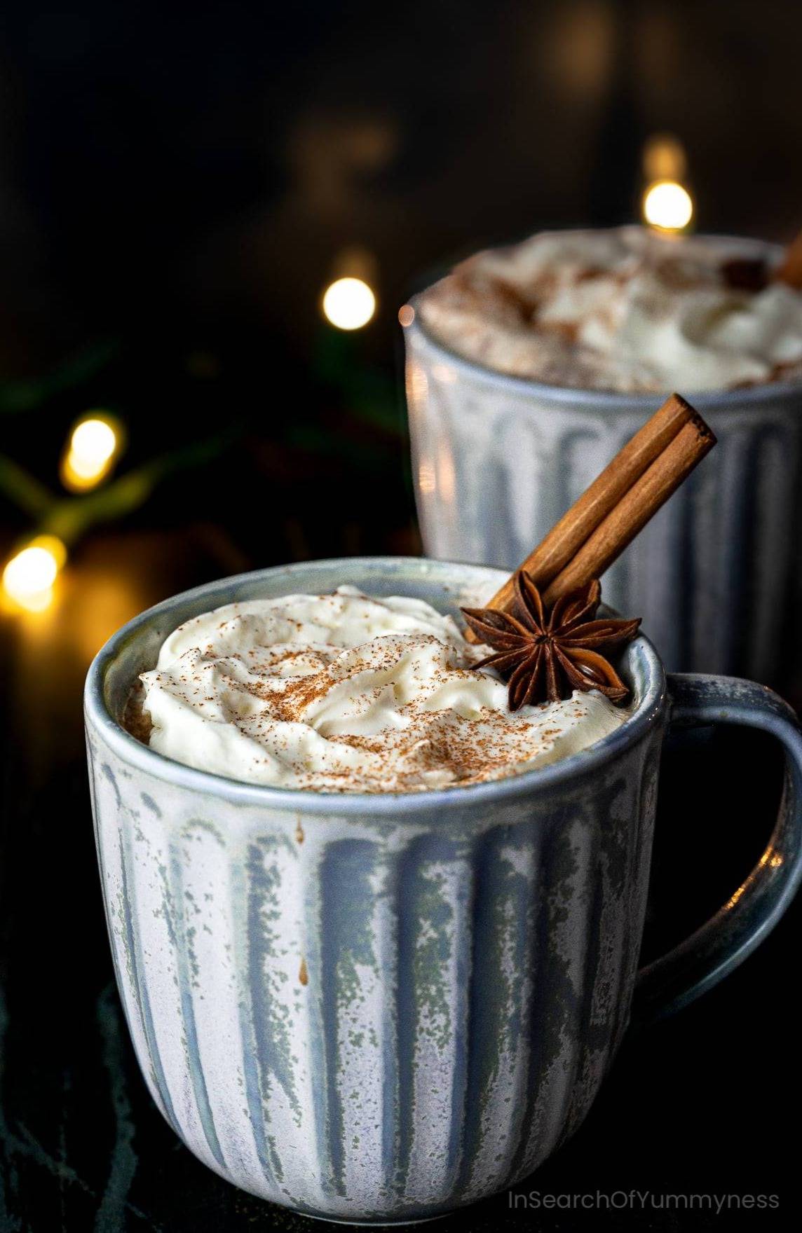 A blue mug filled with spiced hot chocolate topped with whipped cream and cinnamon.