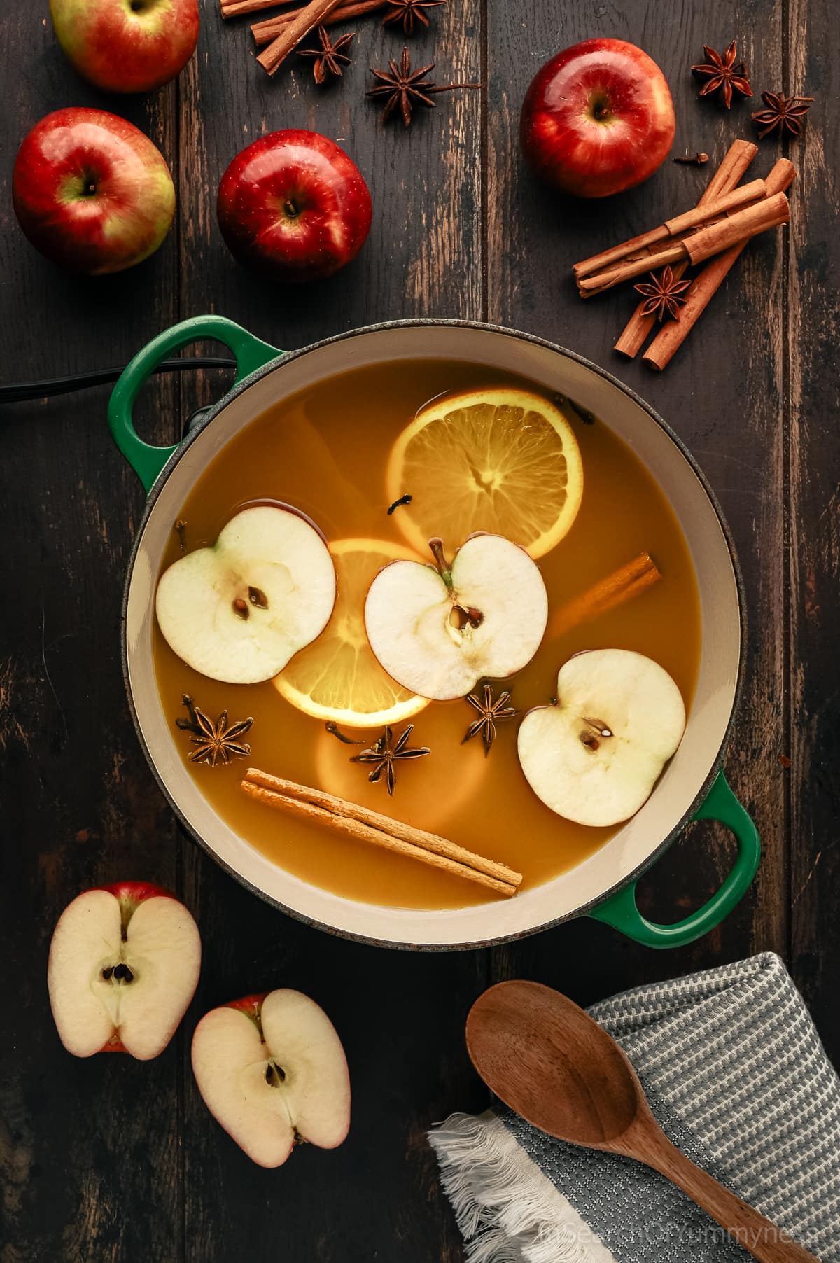 A green dutch oven filled with hot apple cider and apple slices