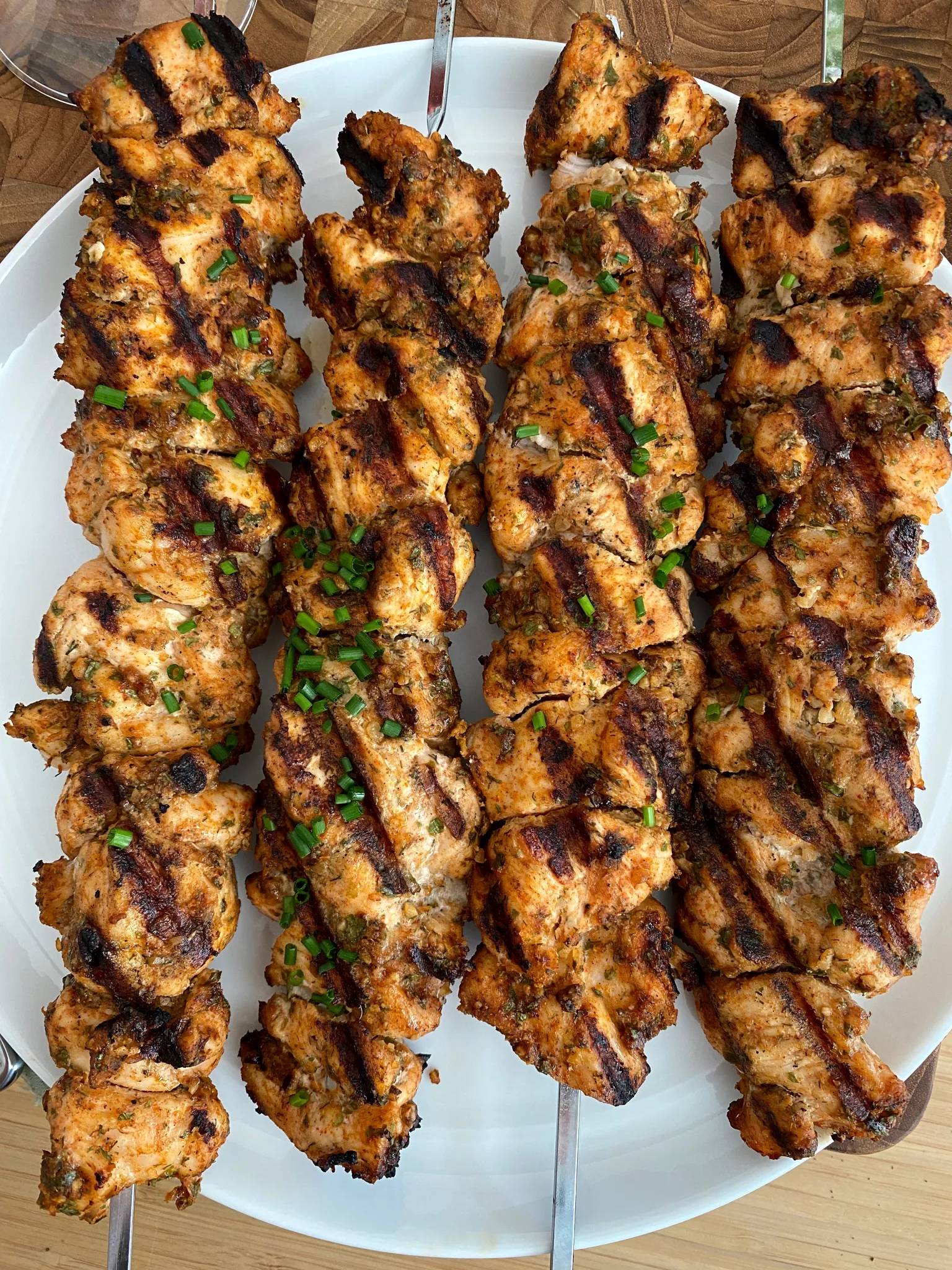 Four spicy chicken skewers on a white platter.