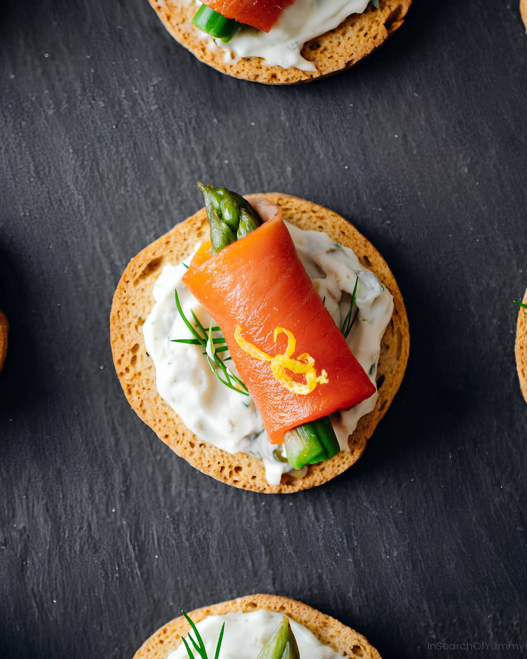 A melba toast topped with a creamy spread, an asparagus spear, and a piece of smoked salmon.