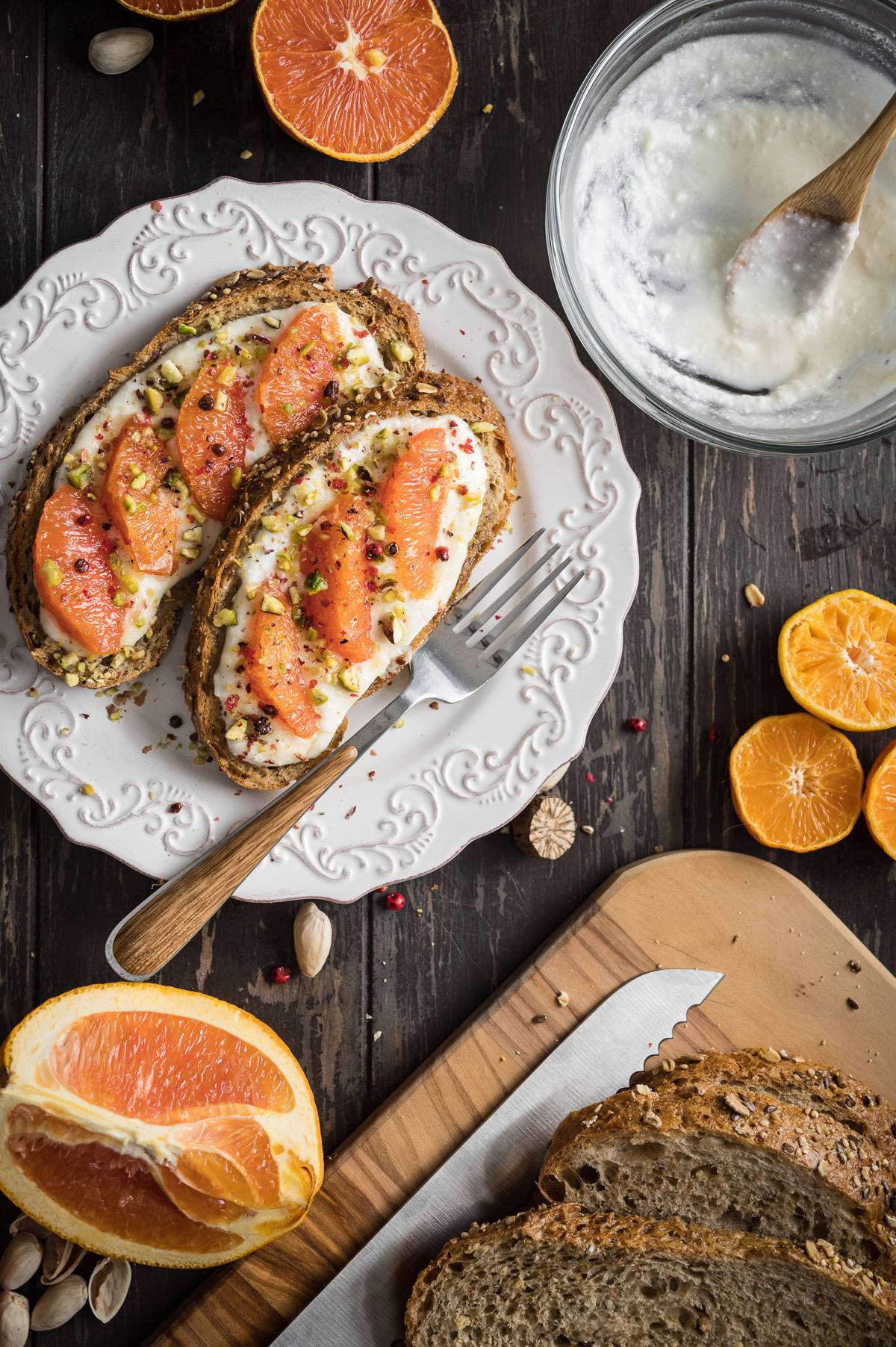 A plate with two slices of ricotta toast next to a cutting board with a loaf of bread.