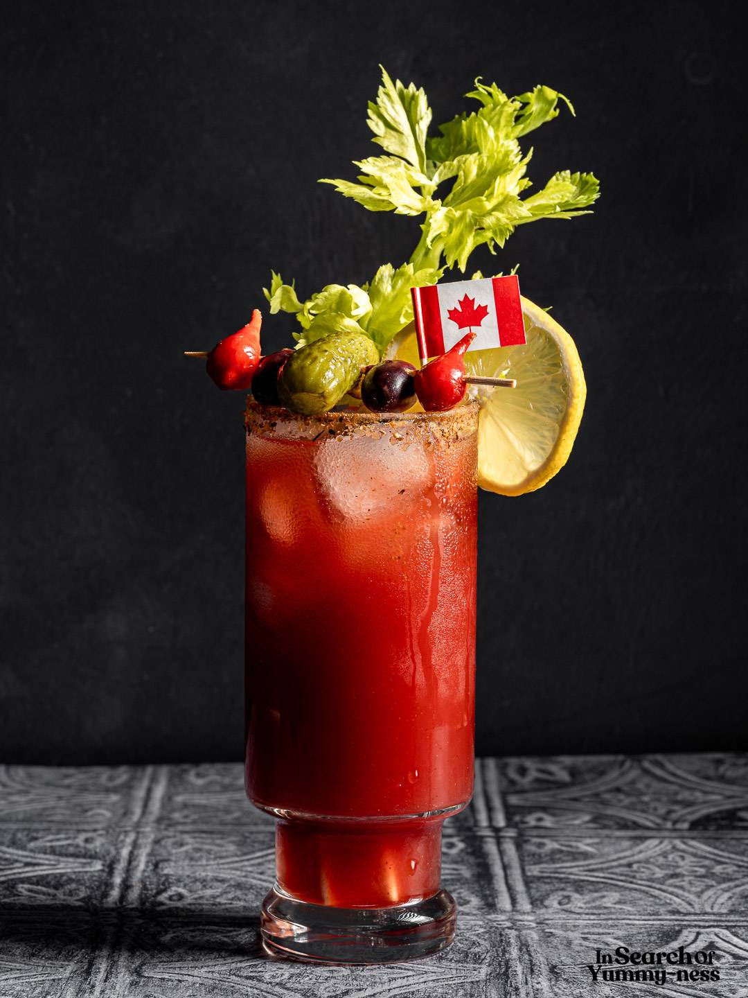 A Canadian Caesar cocktail garnished with a skewer of pickles, a celery stick, a lemon wedge and a mini Canada flag.
