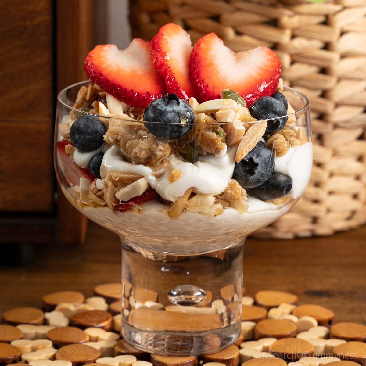A yogurt parfait with granola, almonds, berries and honey in a wide parfait glass.