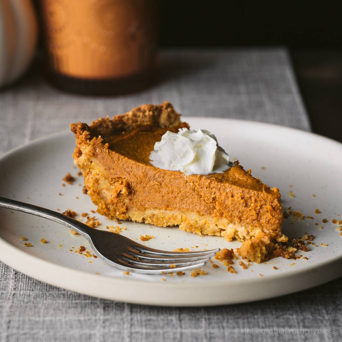 A beautiful slice of pumpkin pie on a white plate next to a fork.