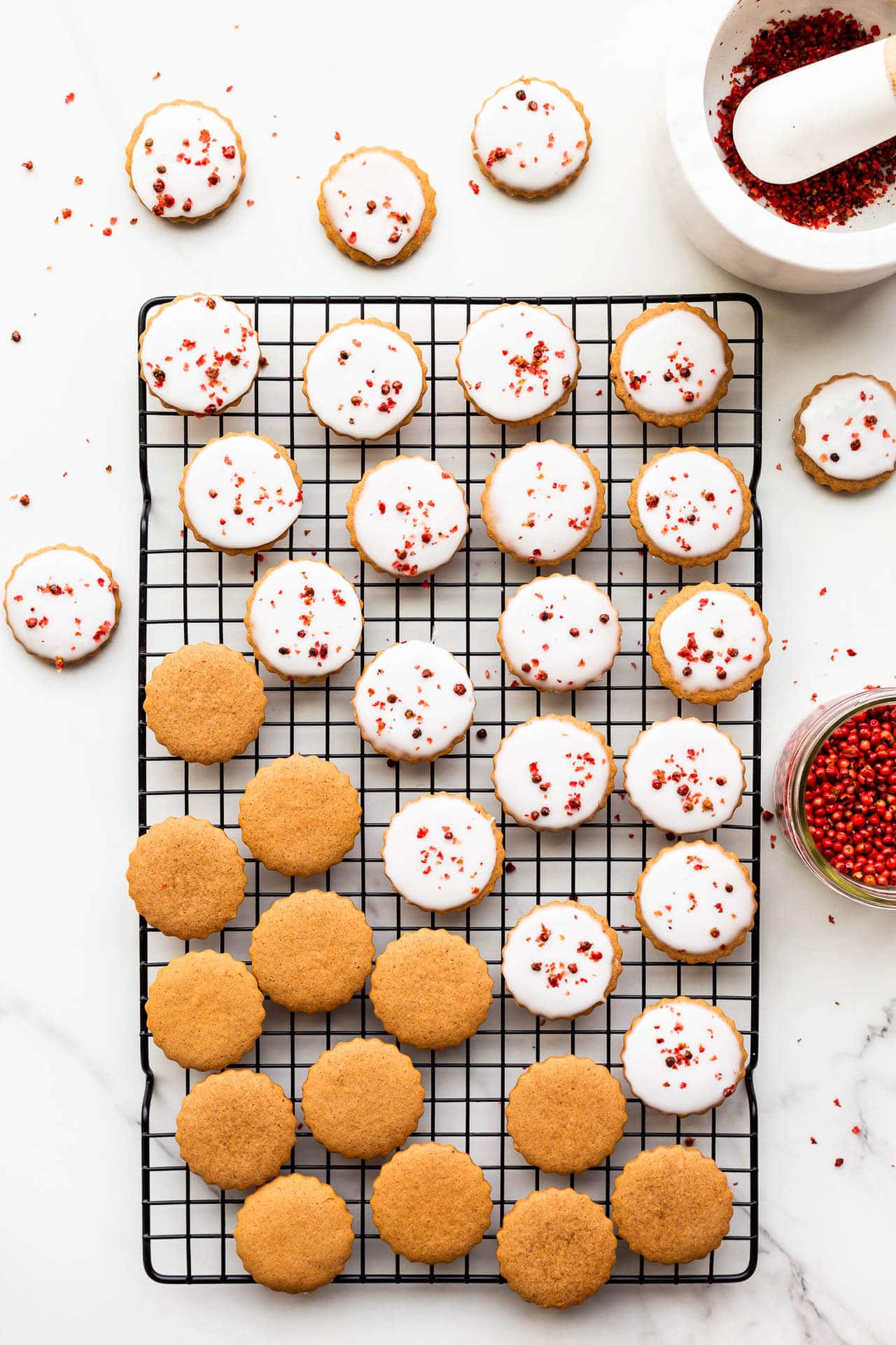 A cooling rack with several round gingerbread cookies on it. Some of them have icing on them.