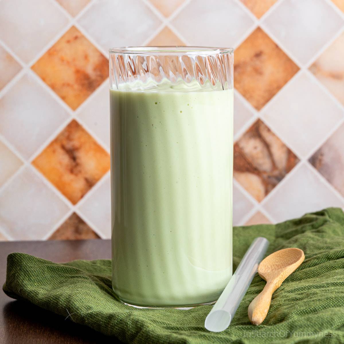 A tall glass of Vietnamese avocado smoothie next to a thick straw and a spoon.