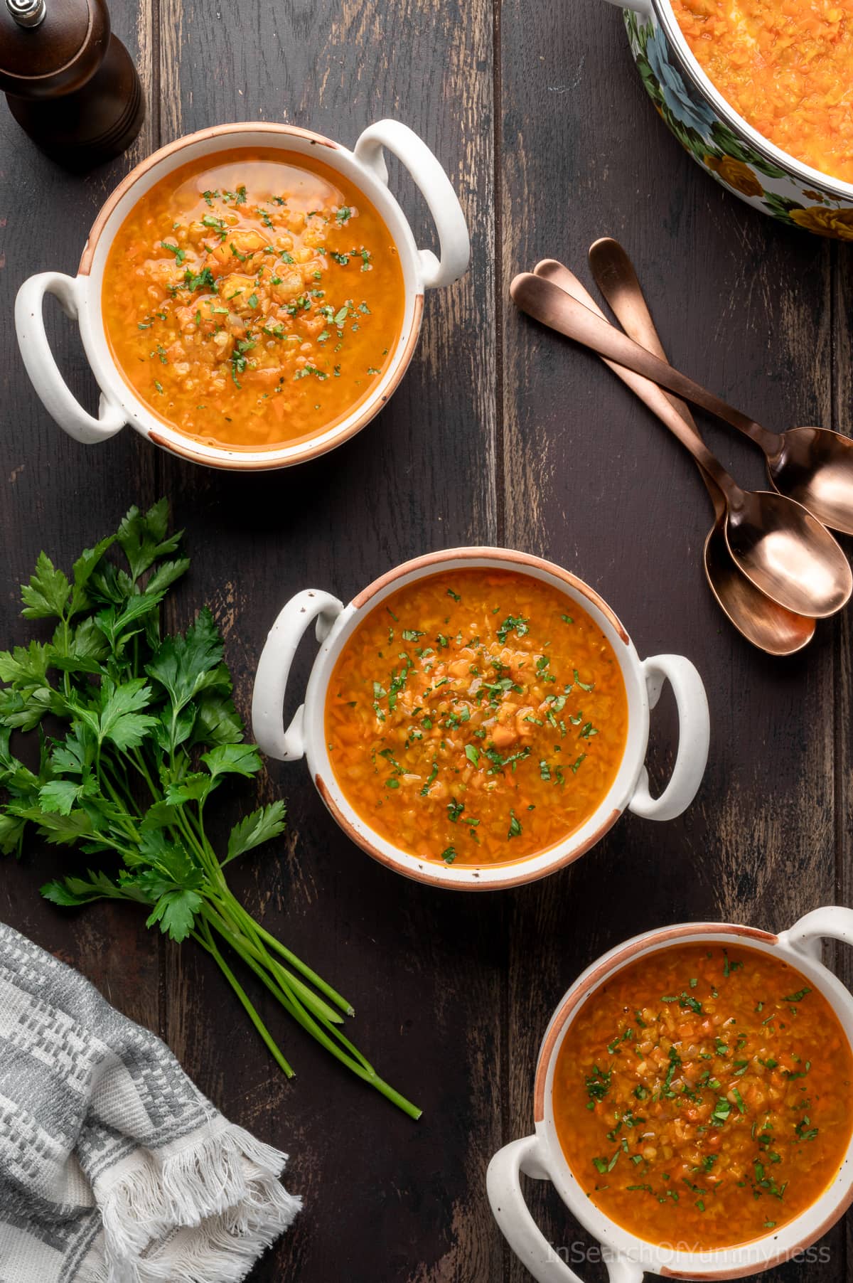 Bowls of lentil carrot soup on a table next to a sprig of parsley.