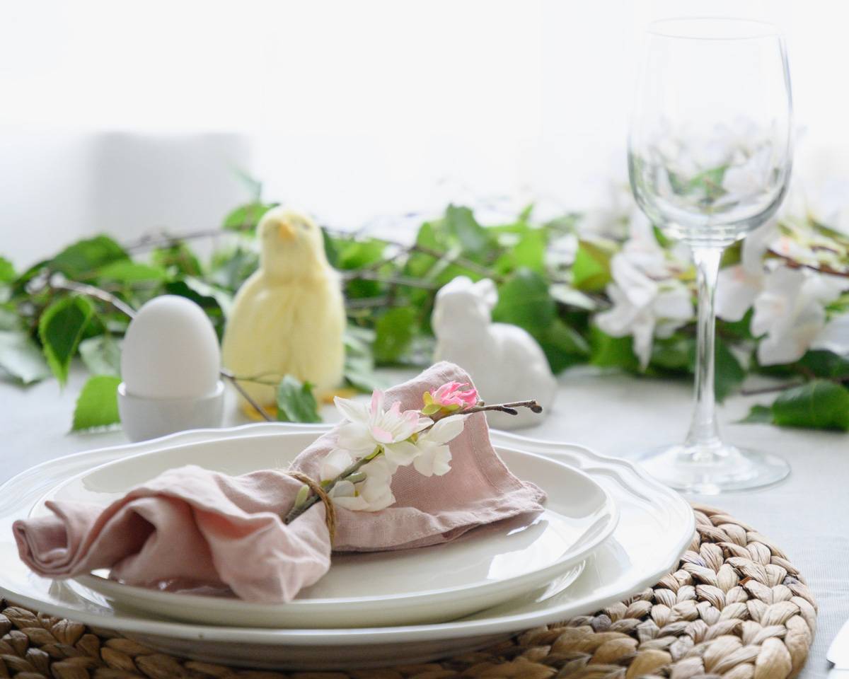 close up of a place setting with a chick, an egg, and a bunny sitting behind with greenery.