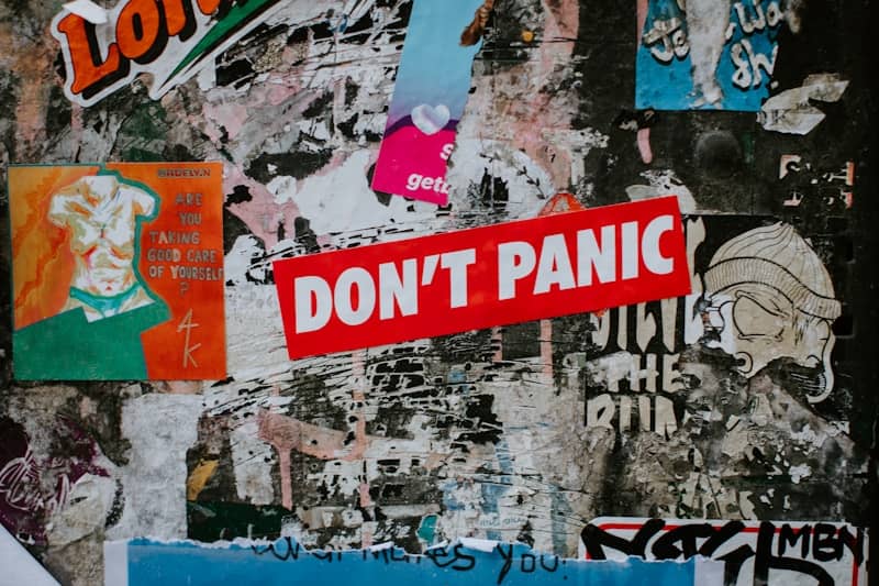 A red "don't panic" sticker on a collage of posters.