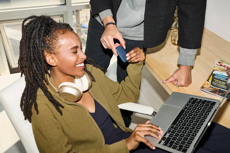 Smiling woman uses laptop, person holds credit card nearby.