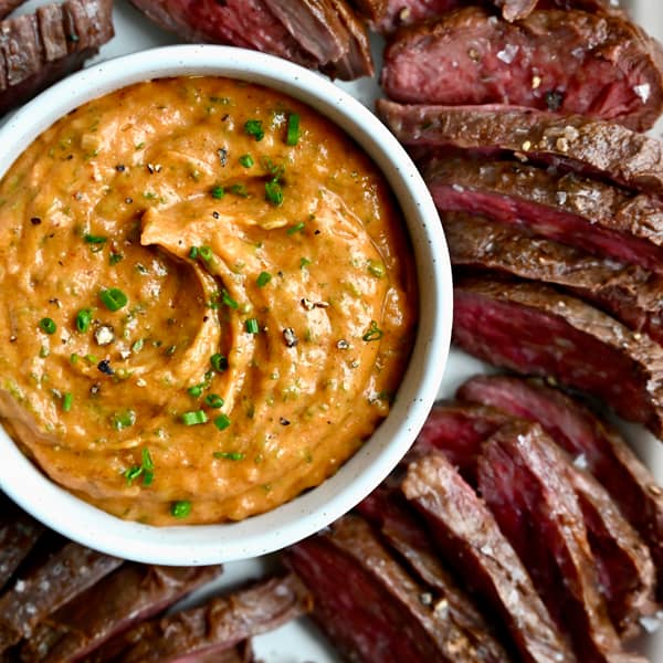 Cowboy butter in a small bowl surrounded by sliced steak.