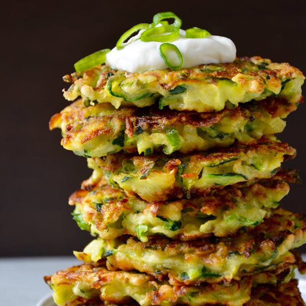 A tall stack of zucchini fritters topped with sour cream.