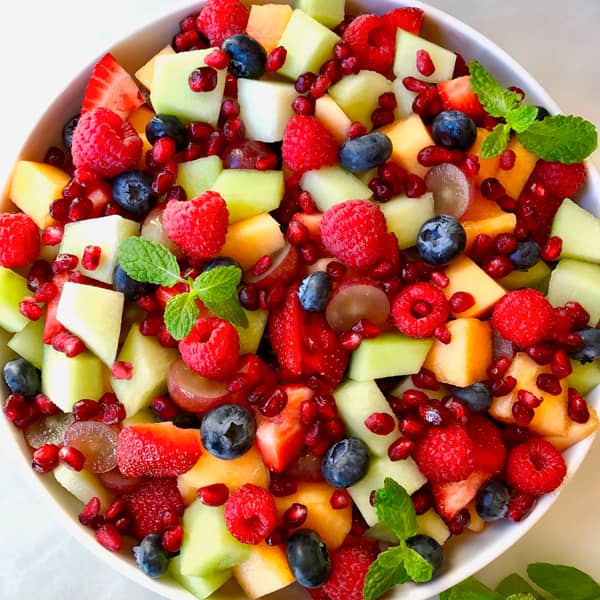 A large bowl containing fruit salad garnished with fresh mint.