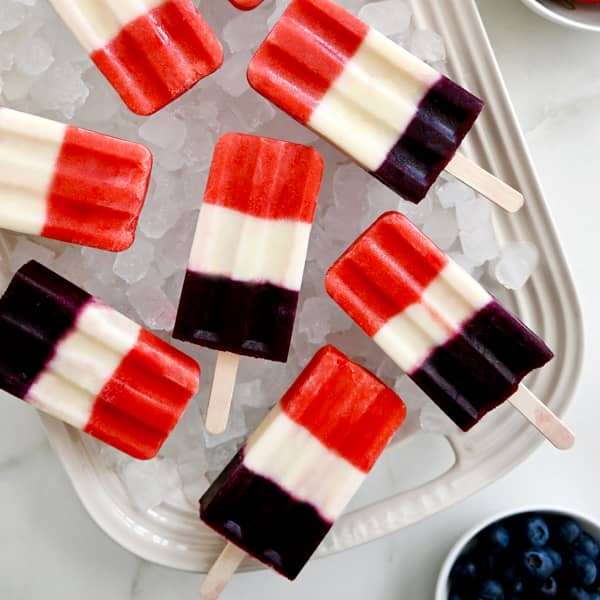 Red, white and blue fruit popsicles over ice on a serving platter.