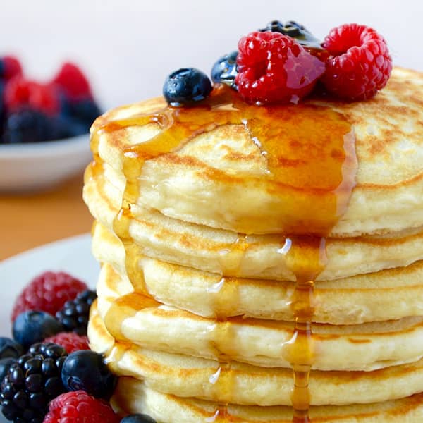 A tall stack of pancakes topped with fresh fruit.