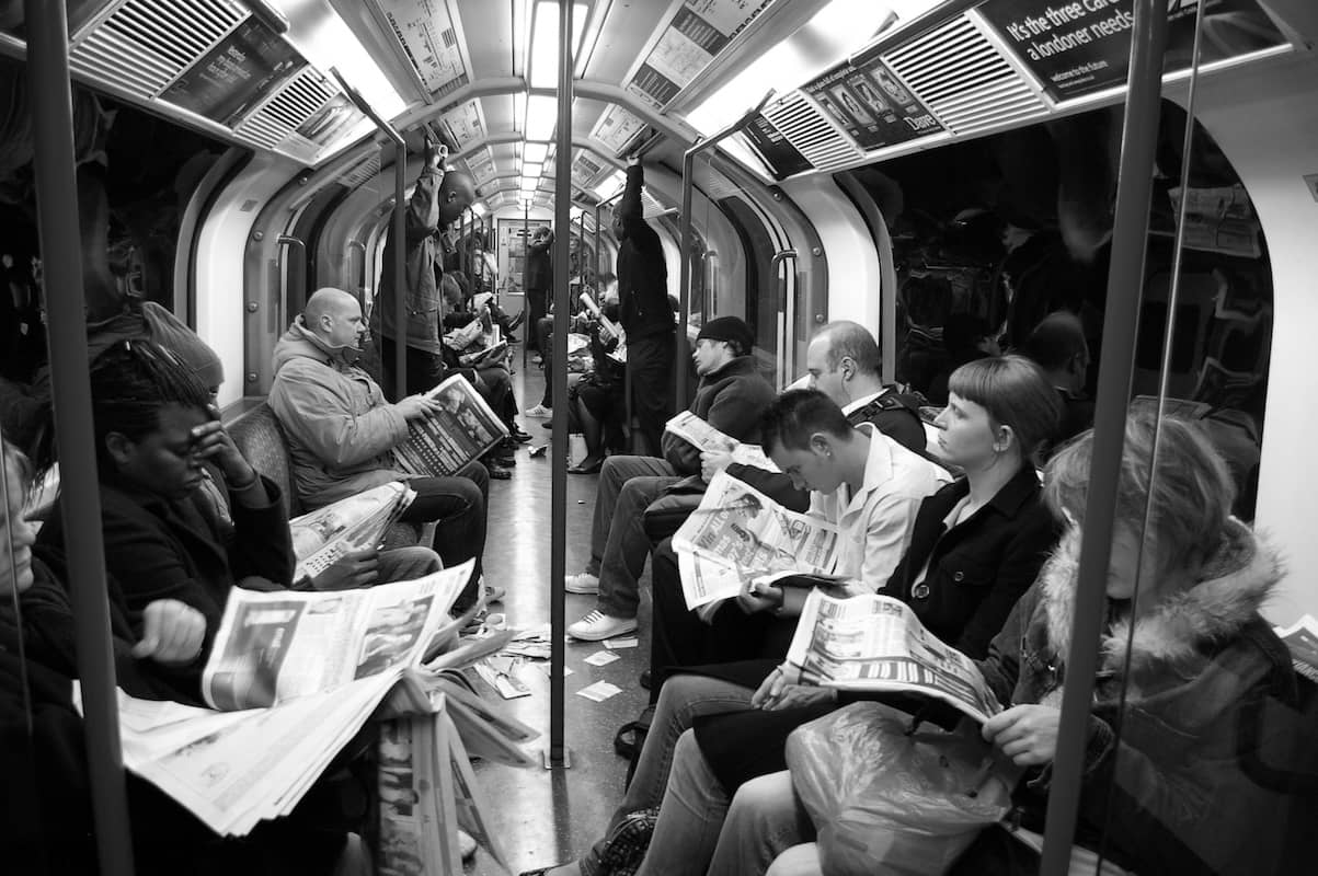 People sit on a subway car reading the newspaper. 