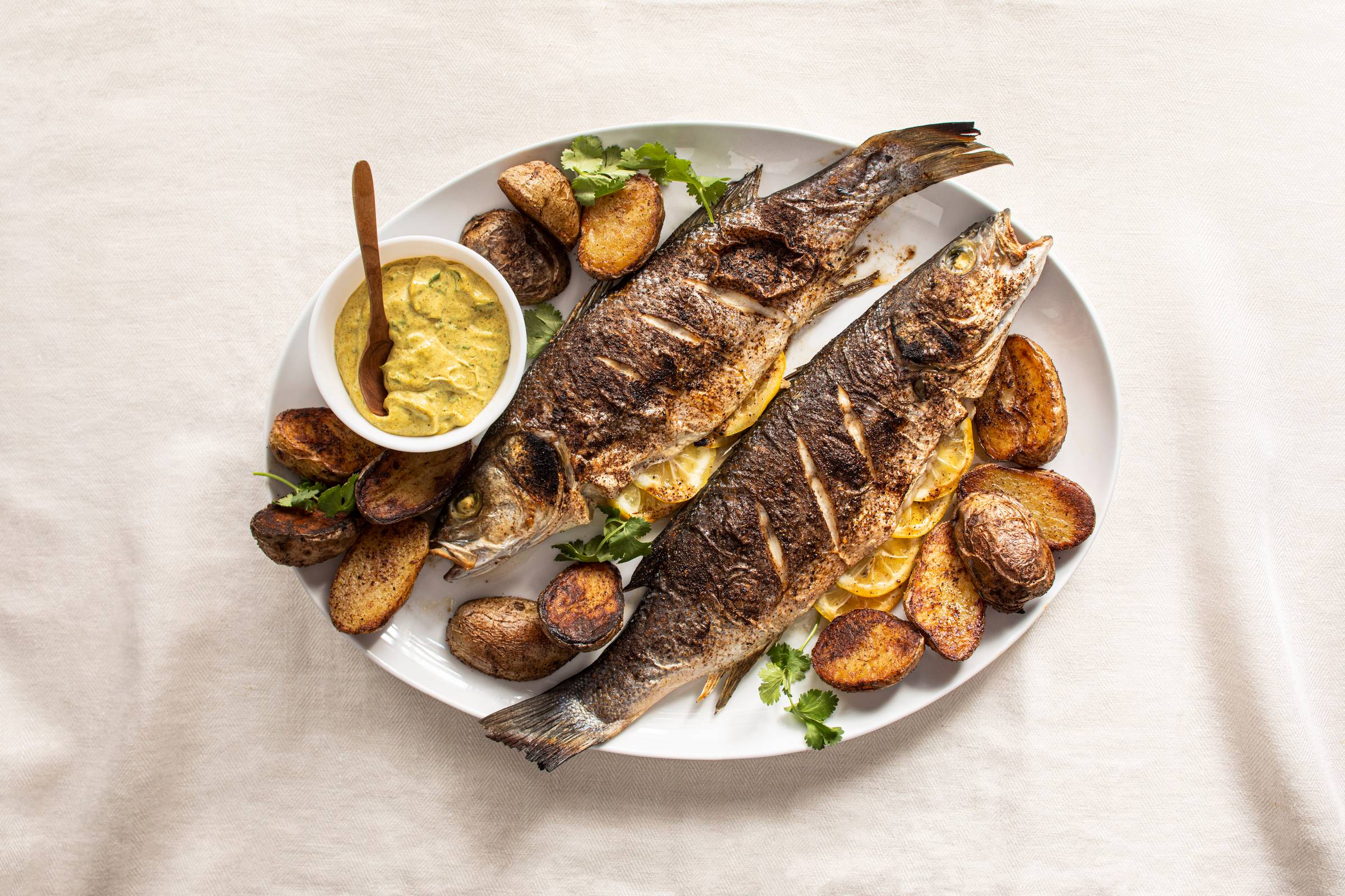 Whole roasted branzino with golden potatoes and curry mayonnaise on a white serving plate