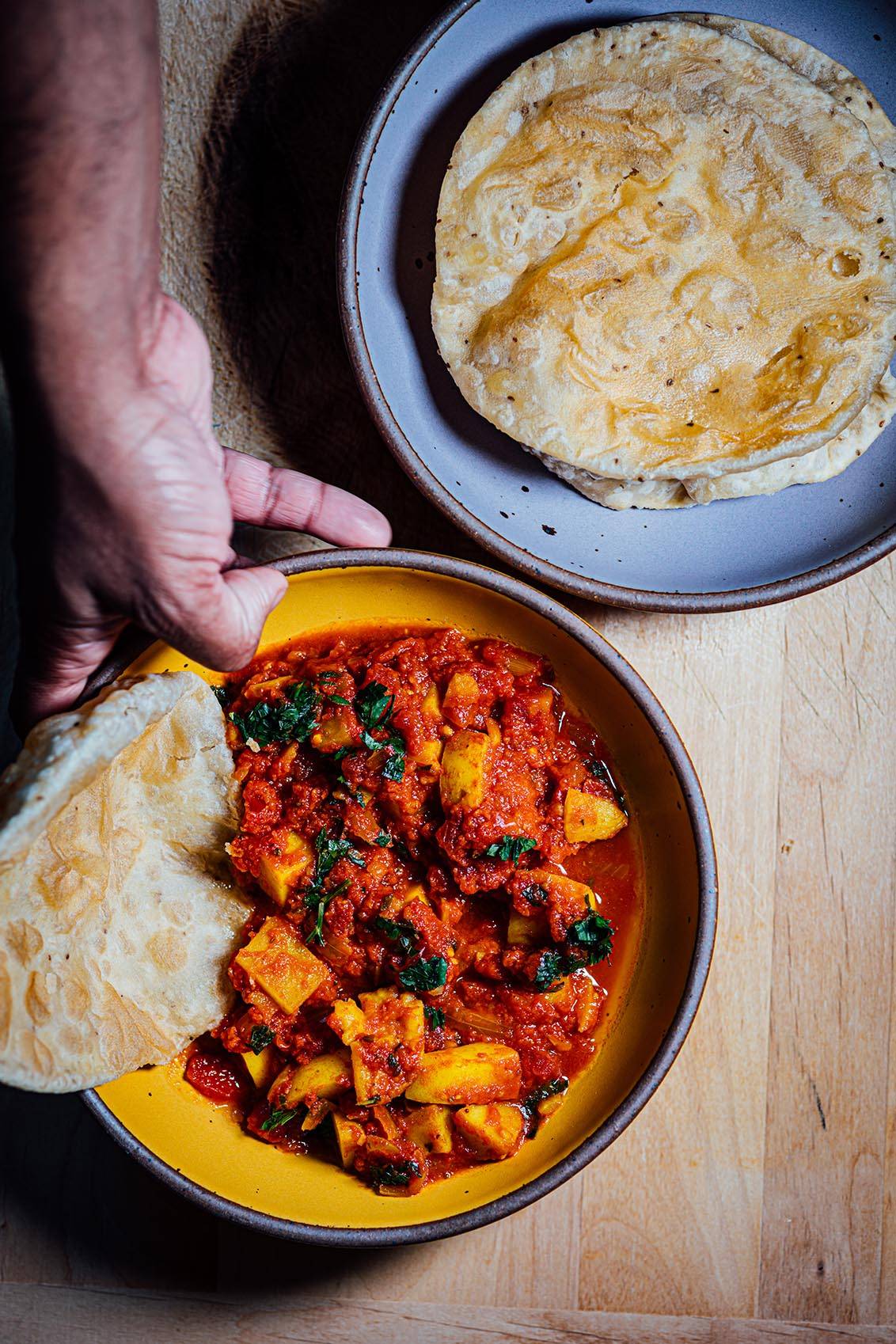 Hand serving fried Indian puris (bread) with tomato and potato gravy