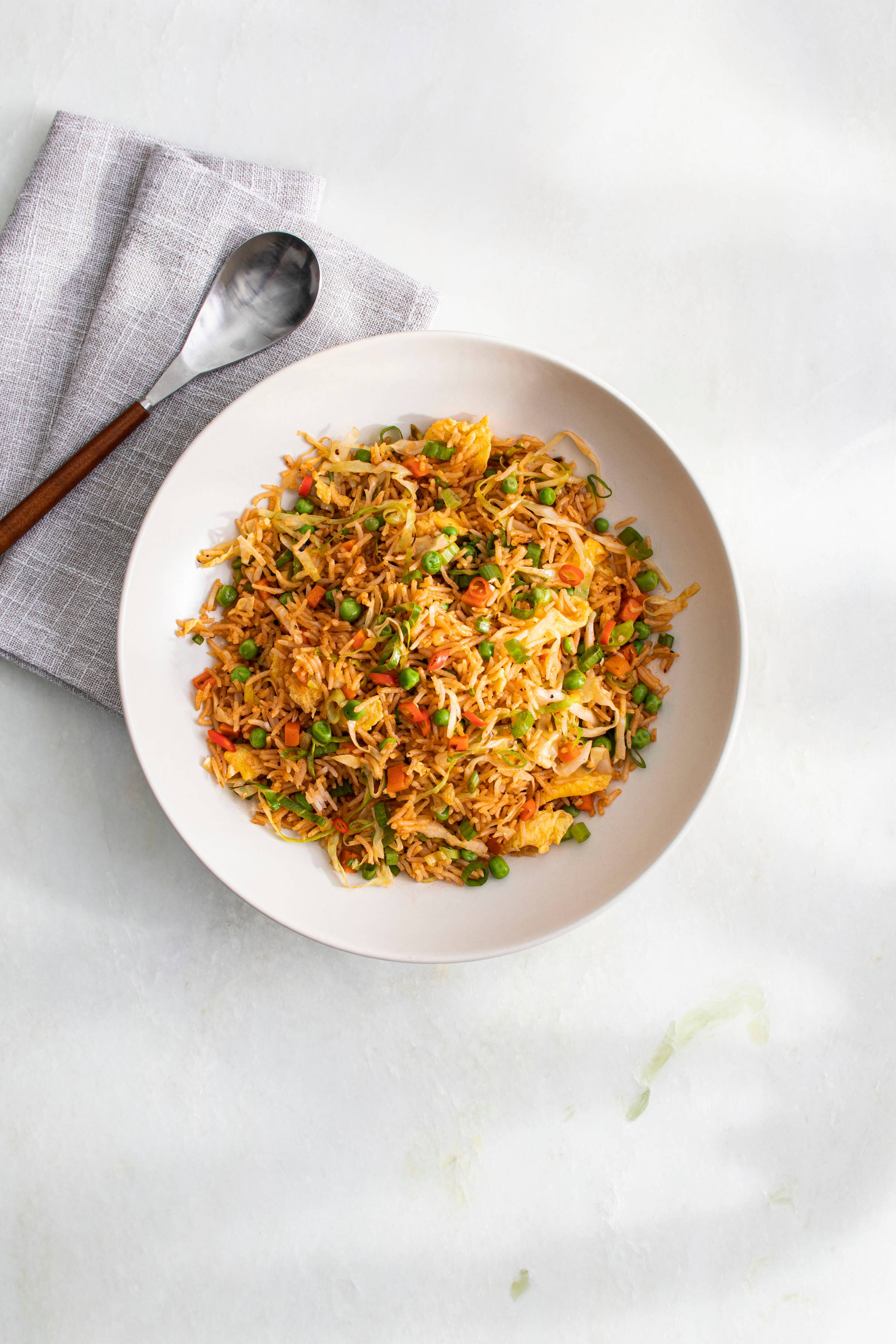 A bowl of Indo-Chinese Ketchup fried rice sitting on a marble table with napkin and spoon