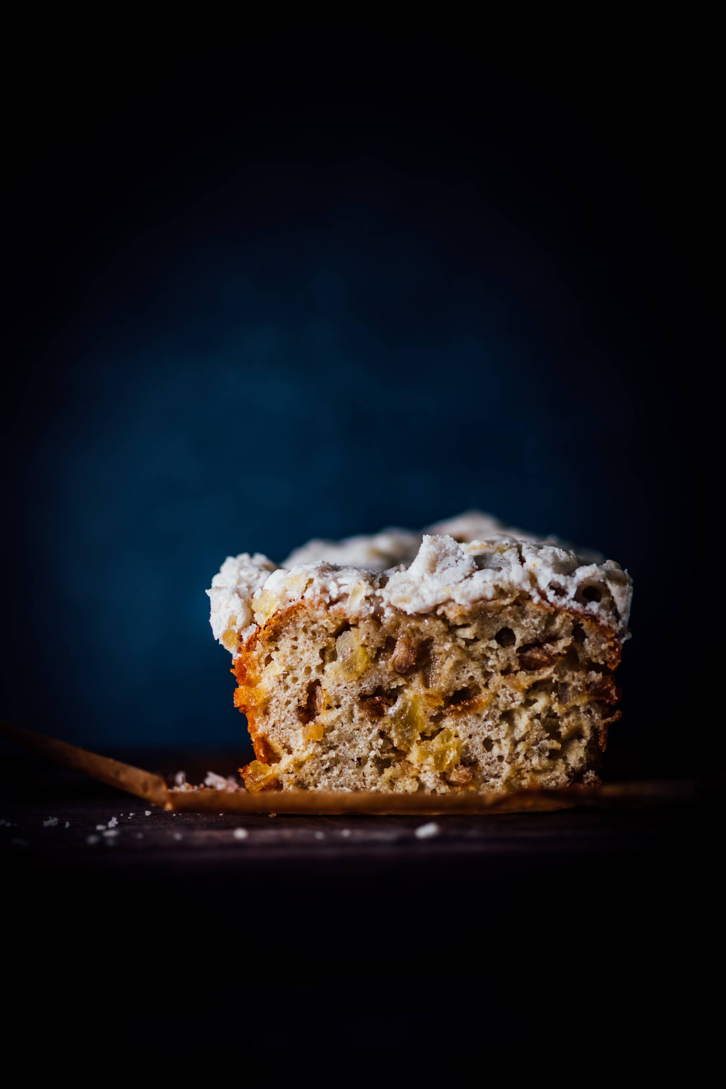 A cross-section of pineapple ginger ras el hanout loaf cake showing a golden crumb studded with crystallized fruit, photographed against a dark blue background.