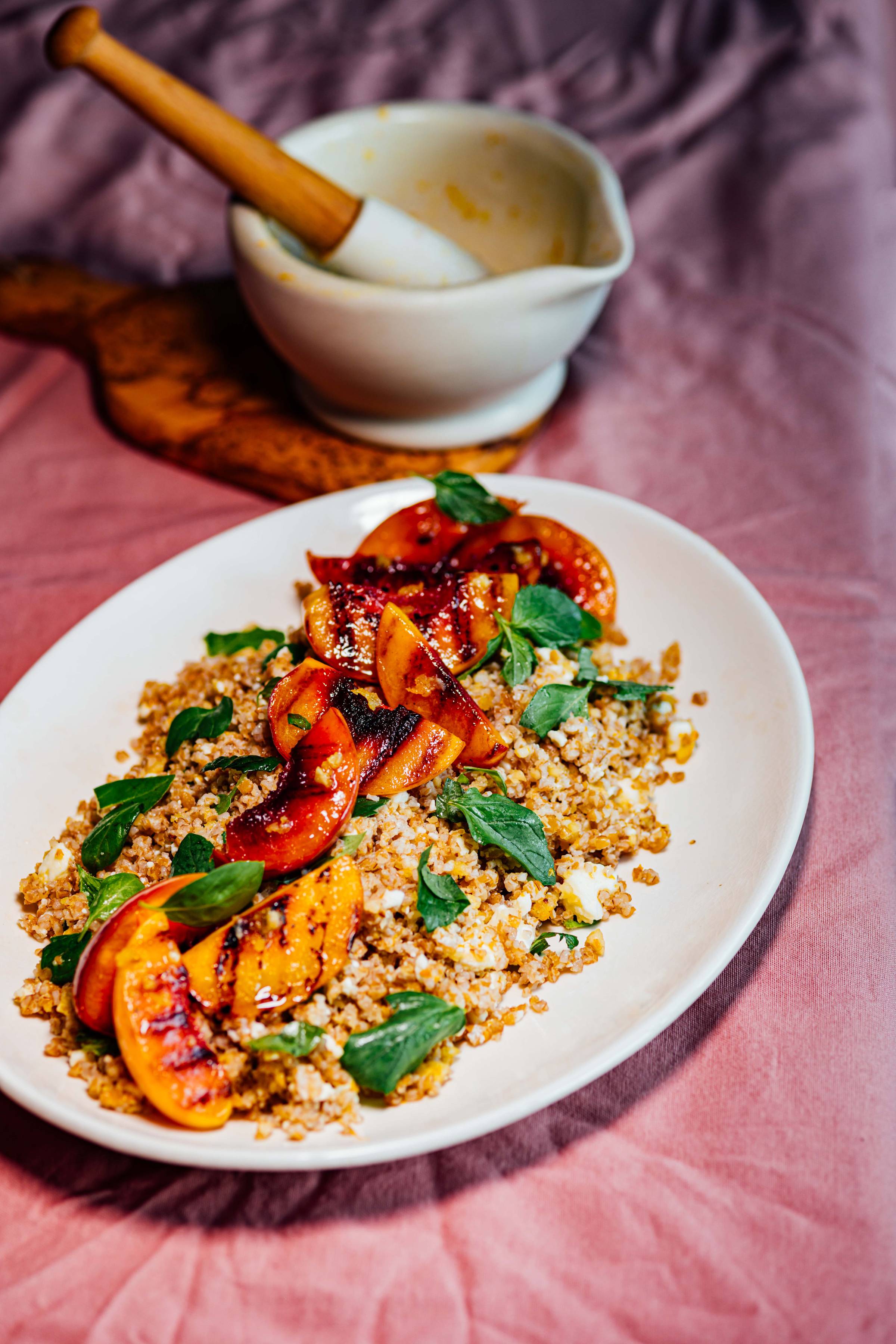 White plate of grilled nectarine bulgur salad with feta and fresh mint, mortar and pestle in the background