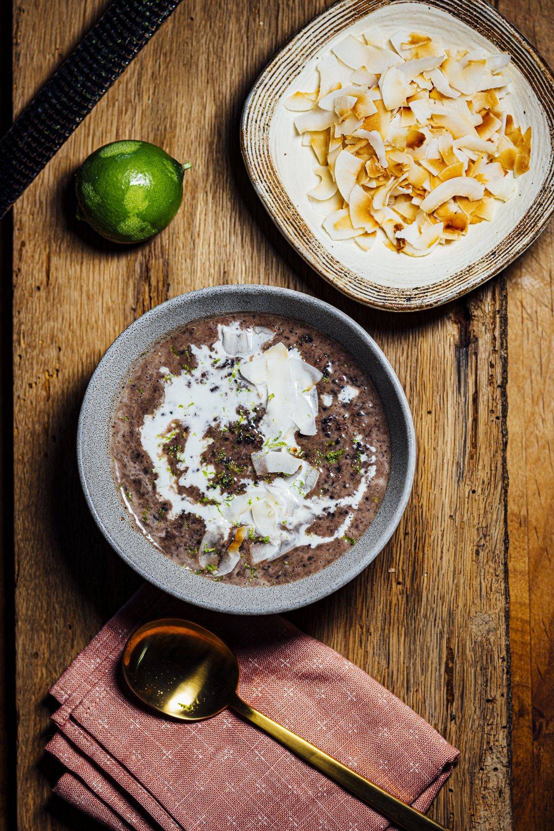 Black rice coconut milk pudding topped with toasted coconut and lime zest, served in a gray bowl on a wooden surface.