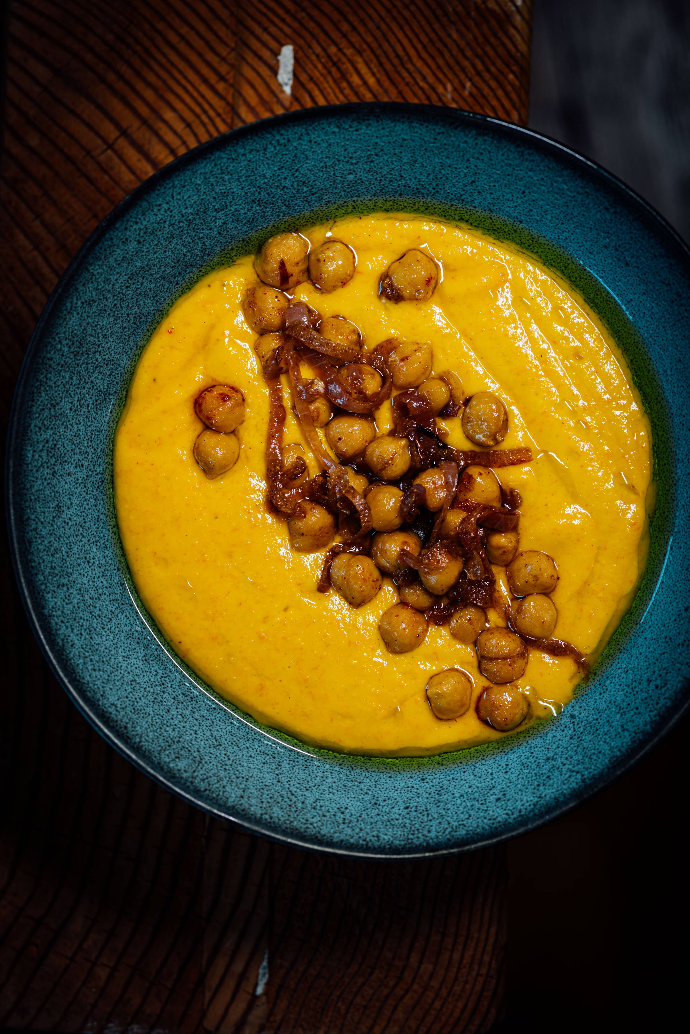 Bowl of chilled tomato soup topped with spiced chickpeas, caramelized shallots, and olive oil.