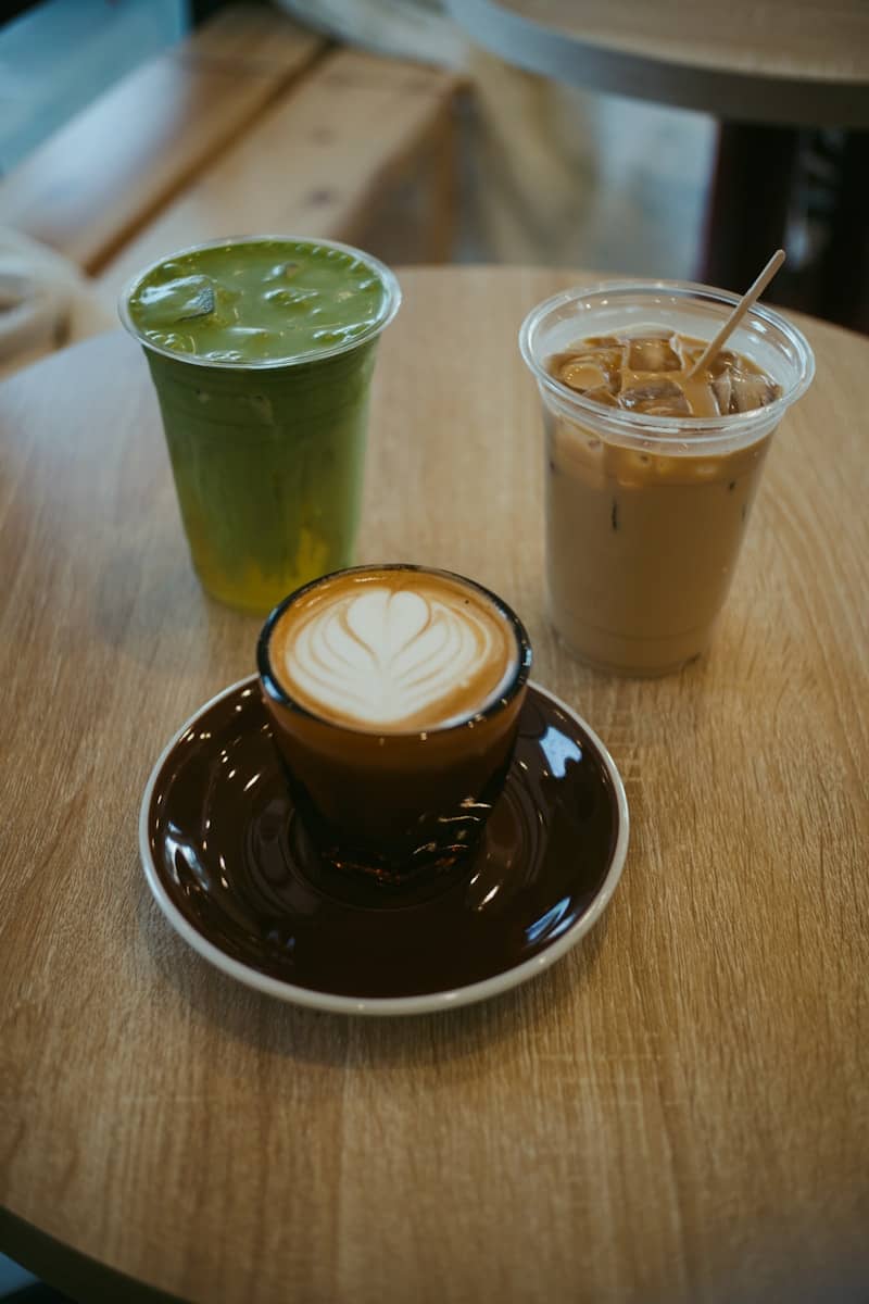 A hot latte with heart latte art, a green matcha drink, and iced coffee