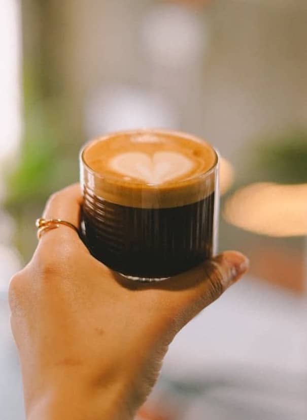 Hand holds a cup of coffee with a heart design.