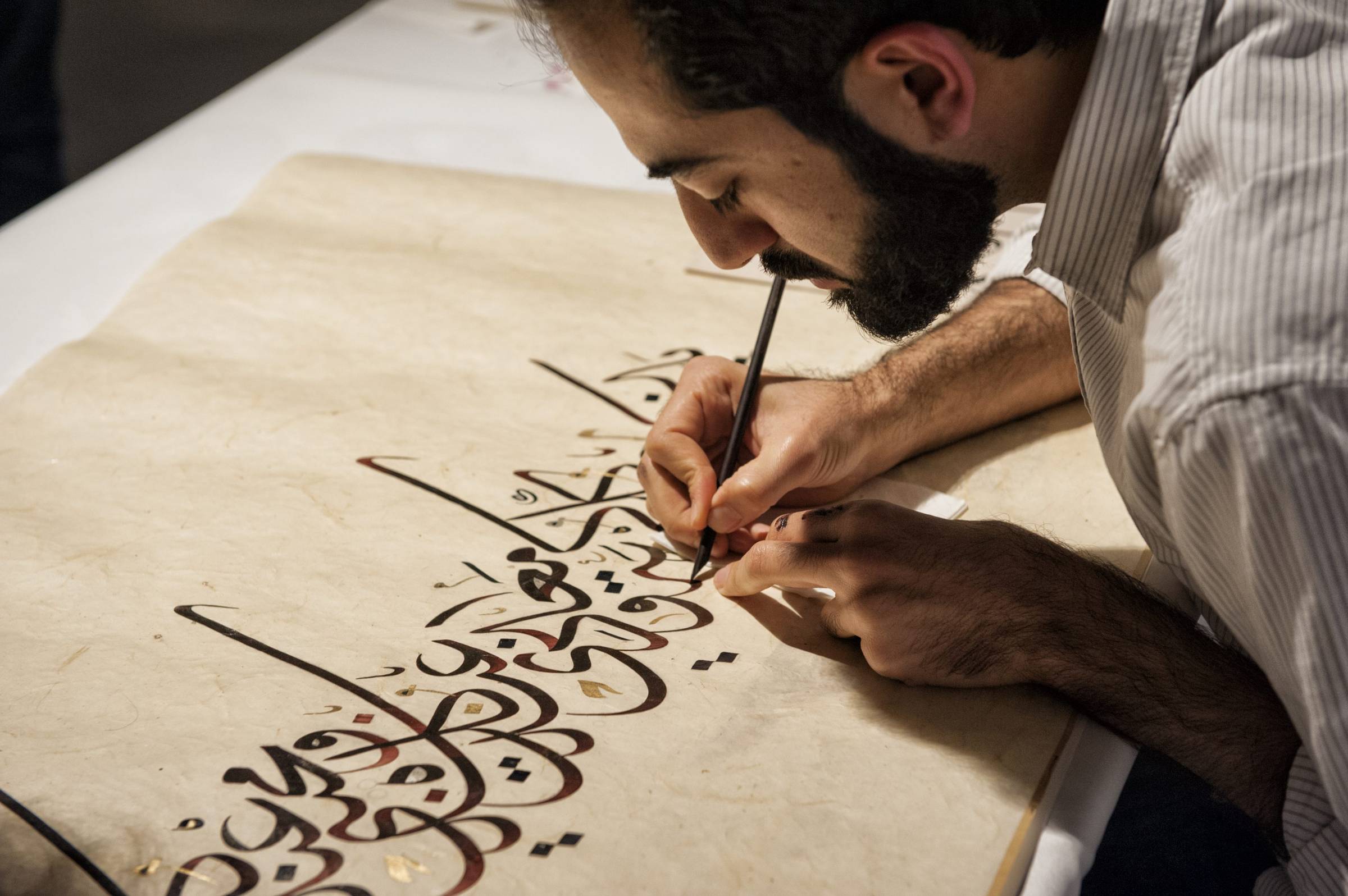 A man writing in Arabic calligraphy on parchment.