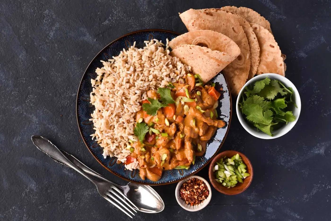 A plate of vegetable tikka masala, rice, and garnishments.
