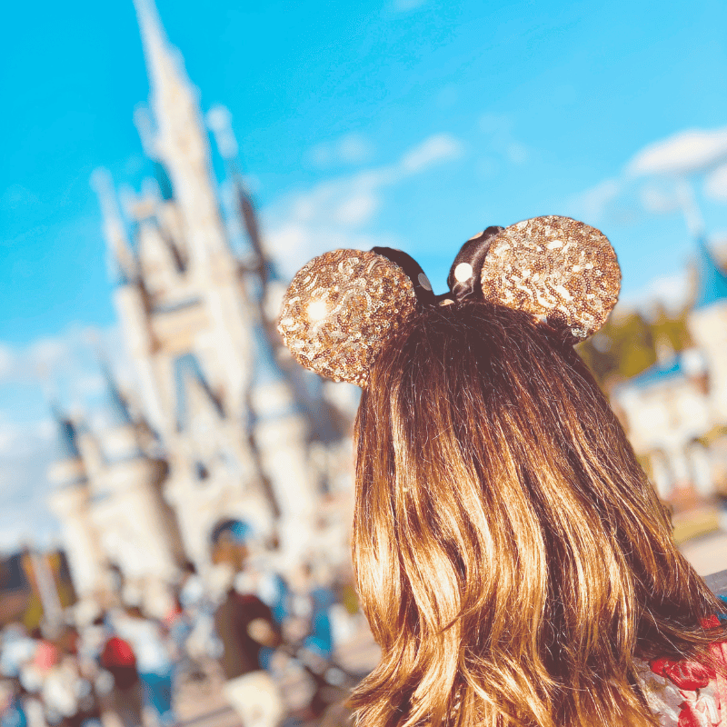 back of a woman in gold sparkly Mickey ears in front of the castle