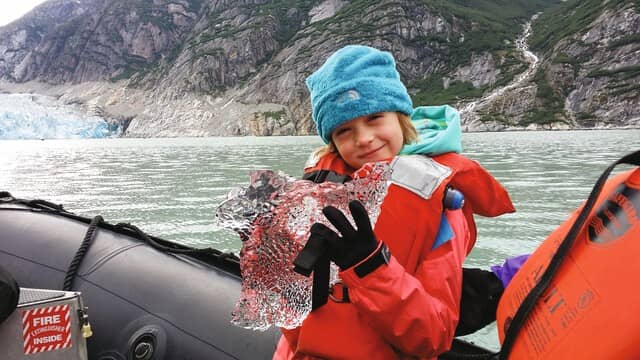 Child in a Zodiac holding a giant piece of ice on a National Geographic Expedition