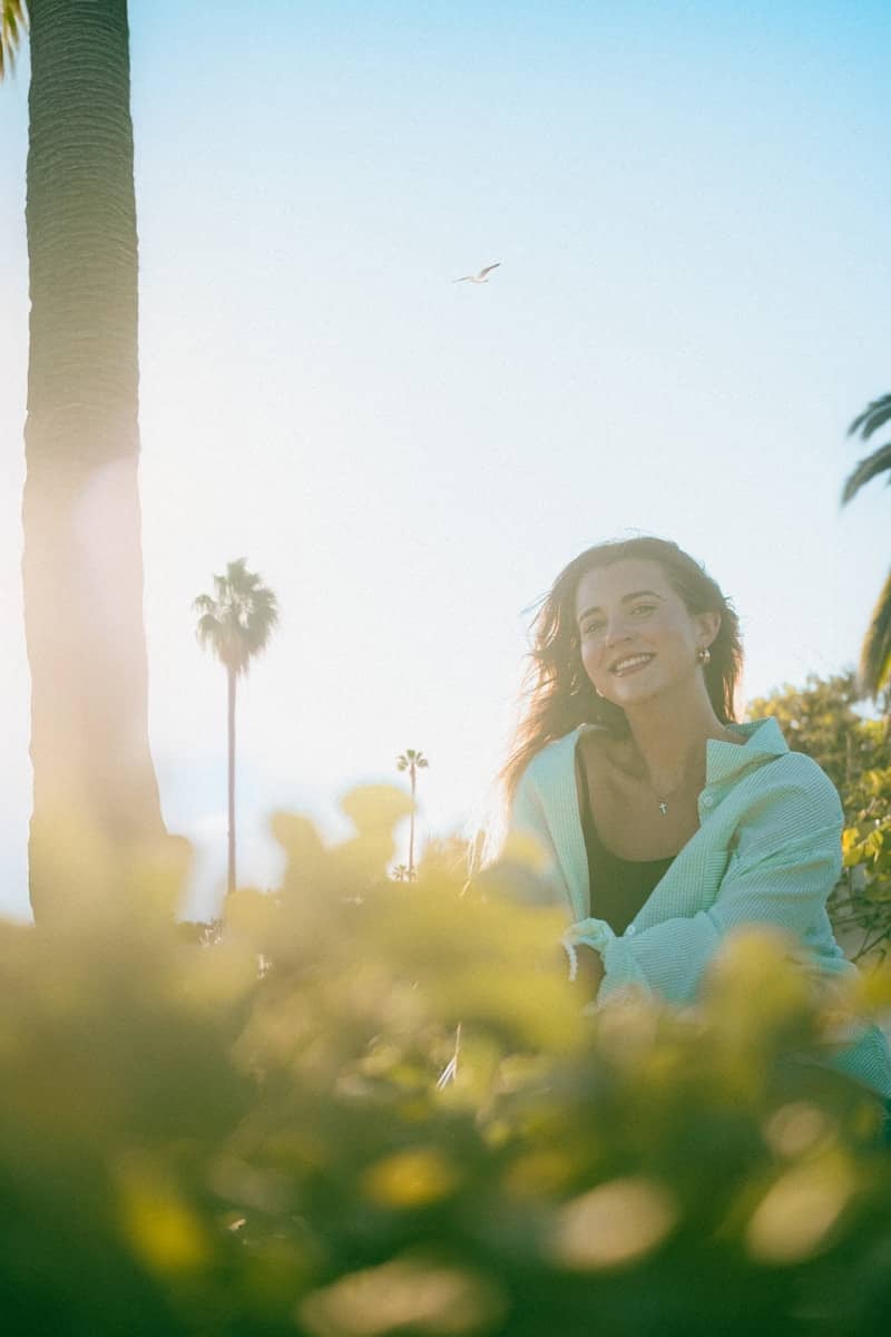 Smiling woman in light blue hoodie outdoors with sun flare