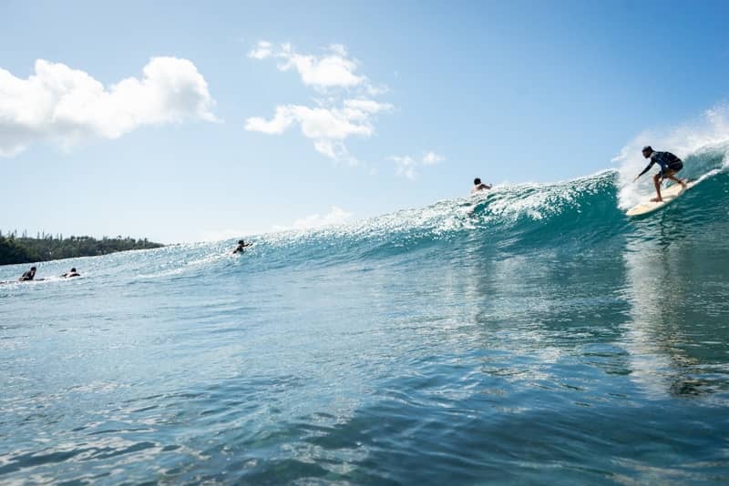Surfers riding a large wave under a clear blue sky