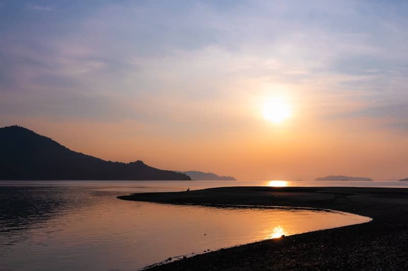 Golden sunset over calm water with distant mountains and shoreline.