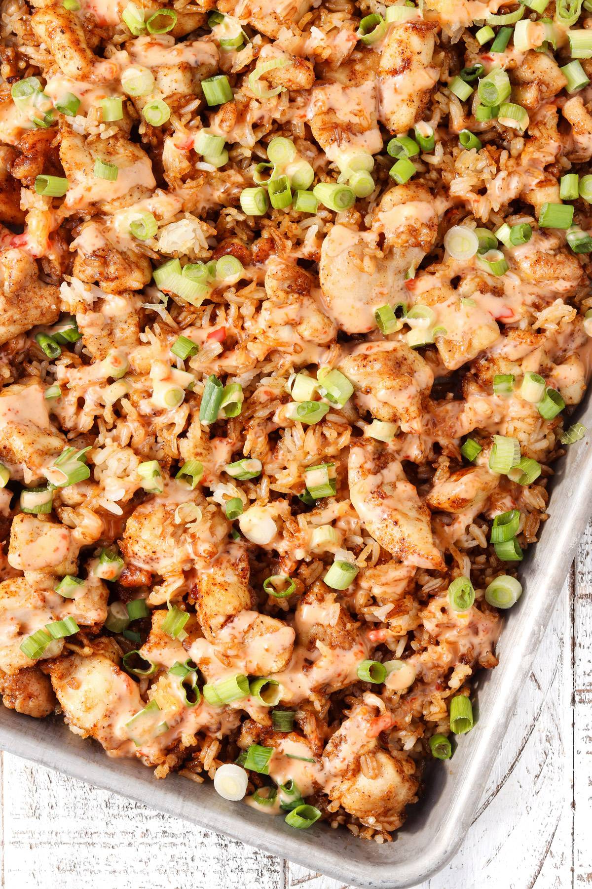 Sheet pan bang bang chicken with crispy rice, topped with sliced green onions and drizzled with creamy bang bang sauce.