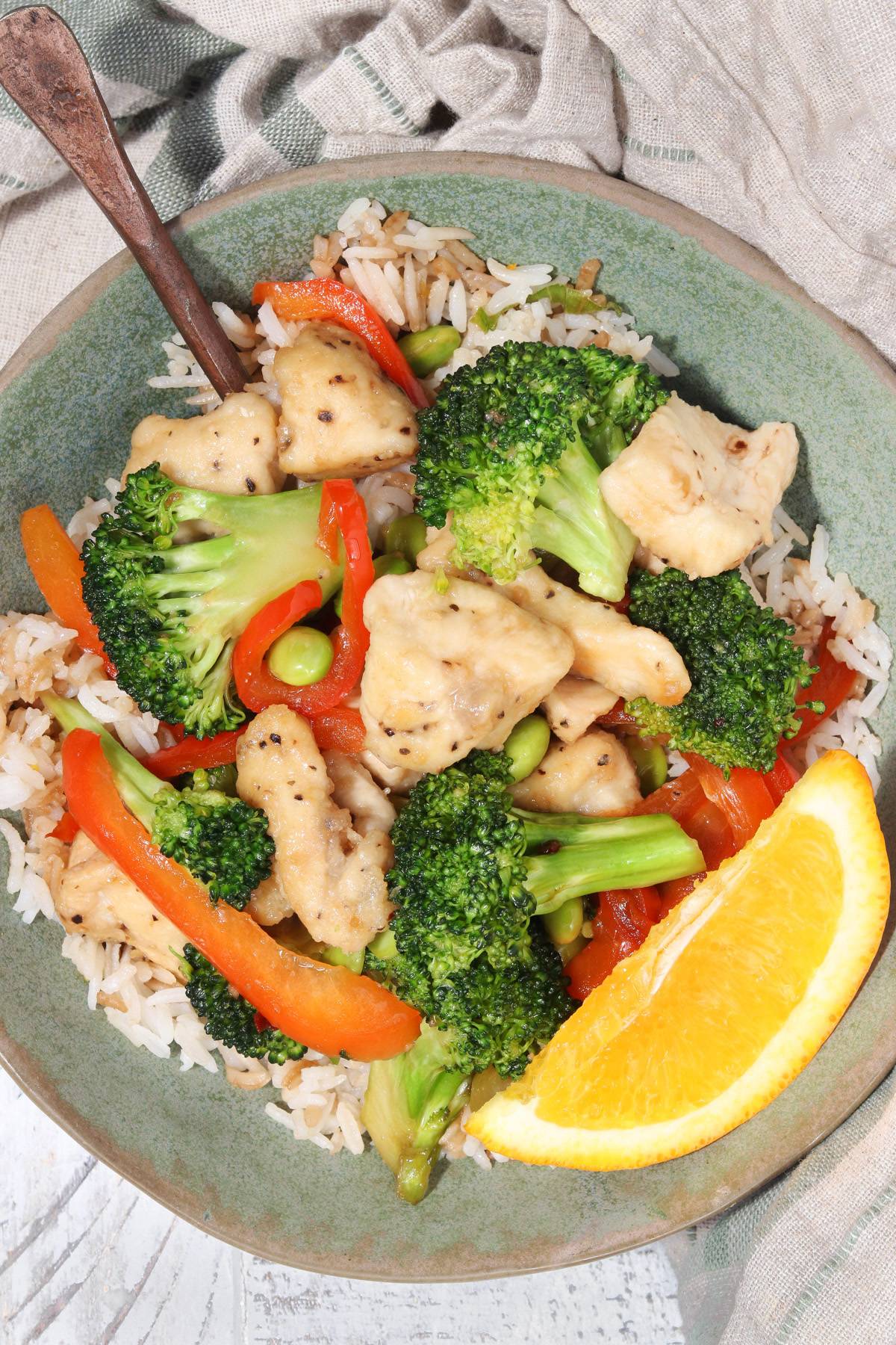 Orange chicken and rice bowls on a white counter garnished with an orange slice. 
