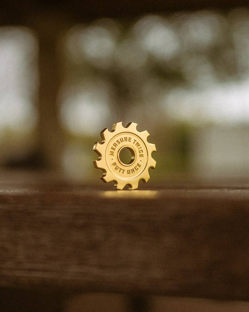 A golden gear pin is sitting on wood.