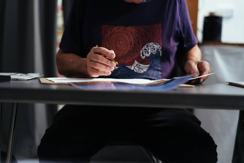 A person in a purple t-shirt holding a pencil over paper at a desk