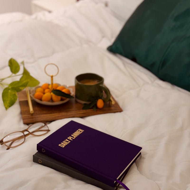 A bed with a tray of oranges and a book on it