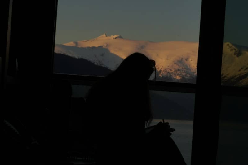A person in silhouette writing in a notebook against a snowy mountain landscape