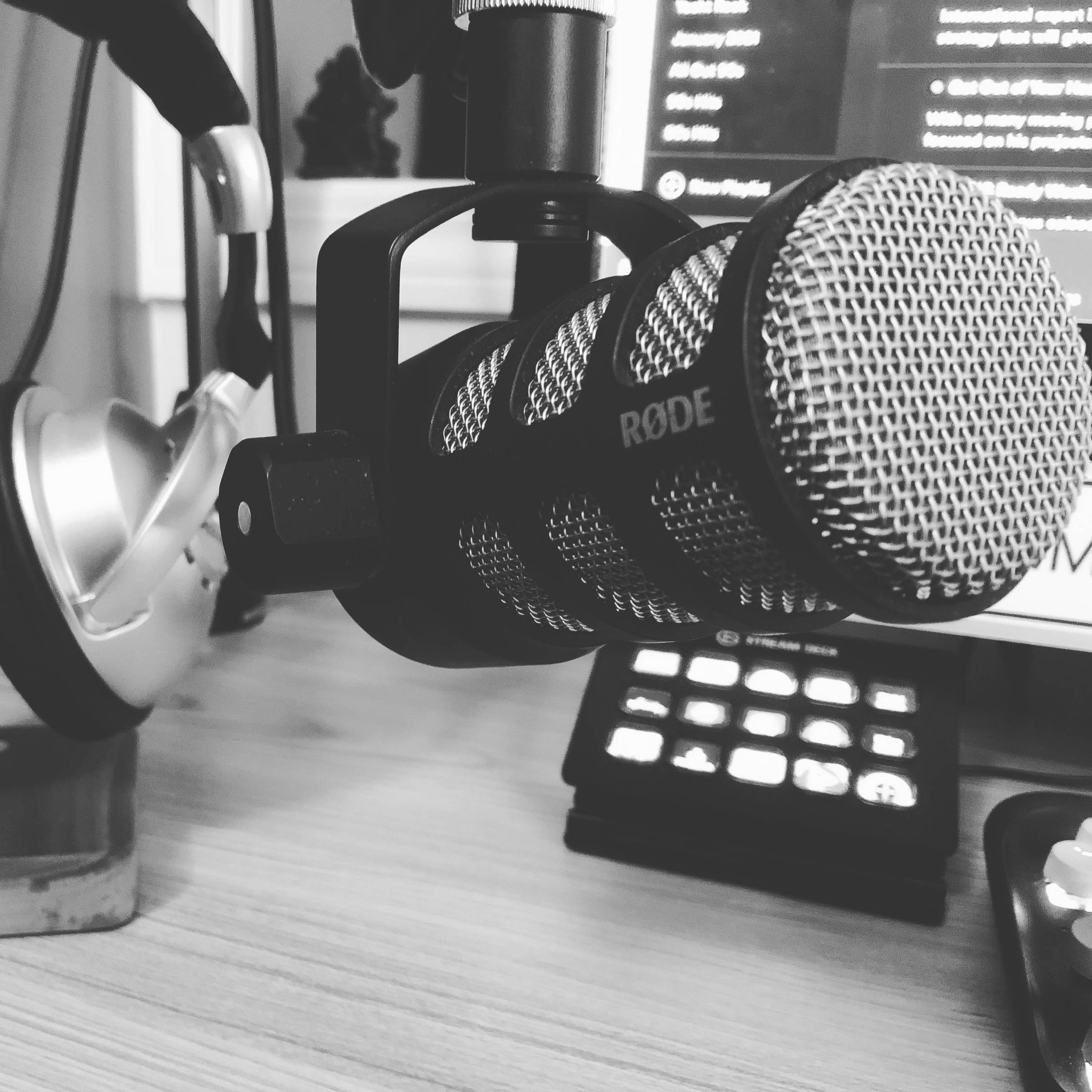A black and white image of a podcast microphone with a set of headphones and a Streamdeck on a desk