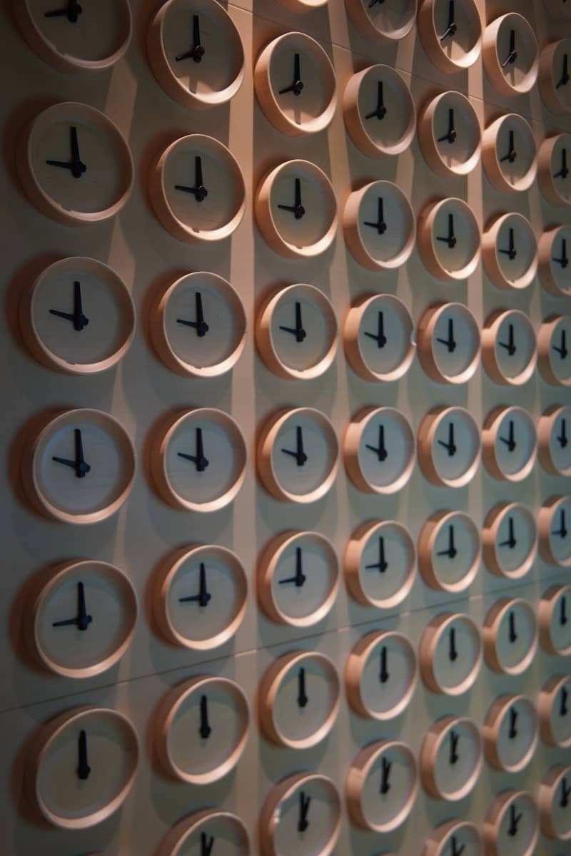 A wall displays a grid of many clocks.