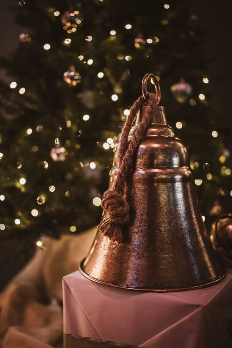 A large bell sits in front of a christmas tree.