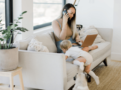 Woman working from home on phone and laptop with toddler and dogs nearby, representing entrepreneurship, work-life balance, and being all in.